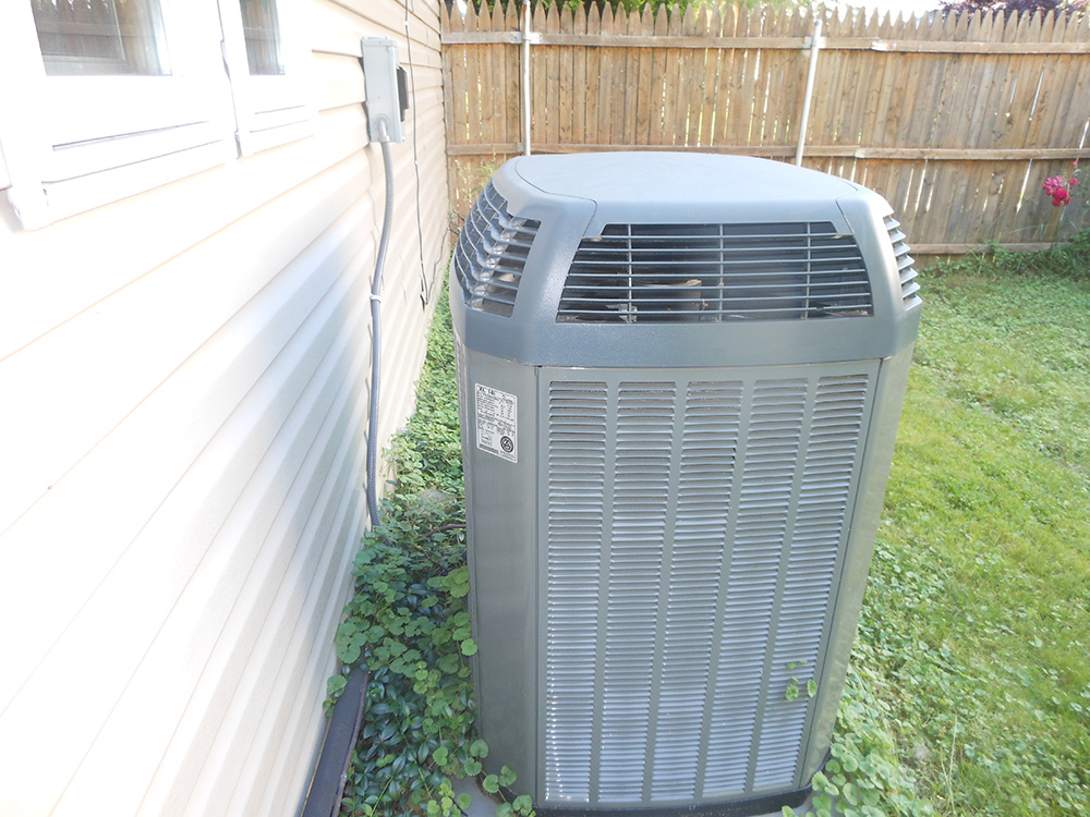 Outdoor central air conditioning unit beside house wall in backyard, efficient cooling system.