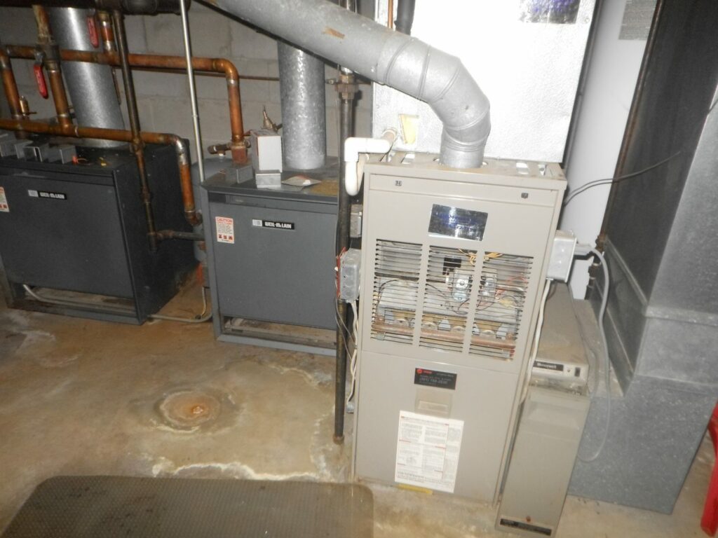 Central air conditioning units in basement with visible pipes and ductwork for efficient home climate control.