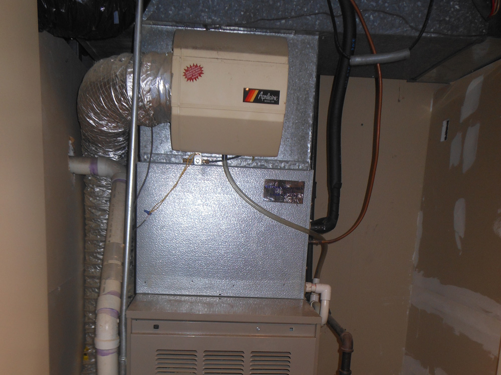 Central air conditioning unit with ductwork and pipes in a utility room.