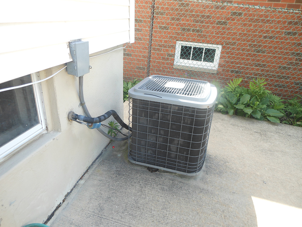 Outdoor central air conditioning unit installed on concrete slab near house wall.