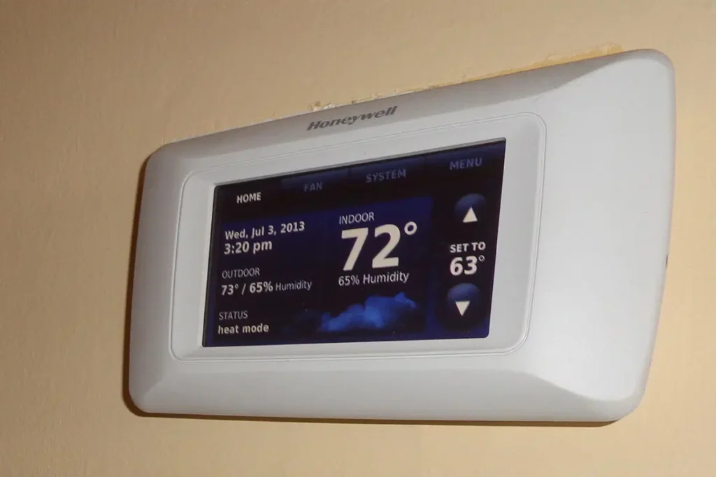 Digital thermostat displaying indoor temperature of 72 degrees with humidity, set to 63 degrees, on beige wall.