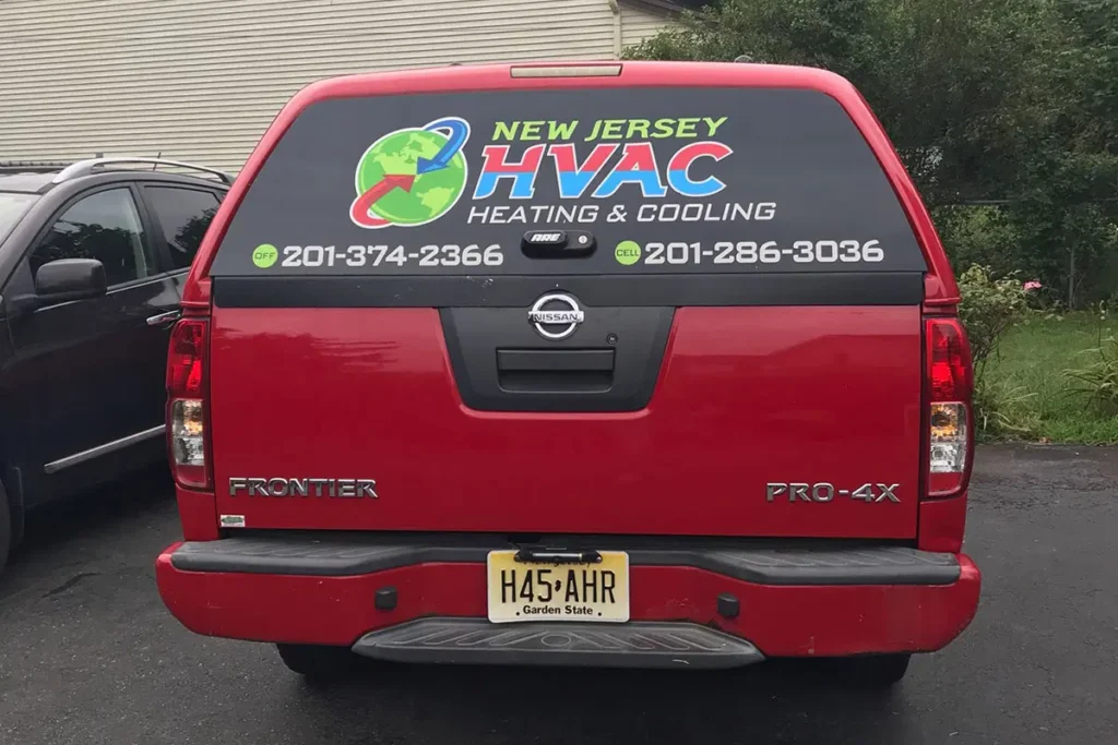 Red Nissan Frontier truck with New Jersey HVAC Heating & Cooling advertisement and contact numbers on rear window.