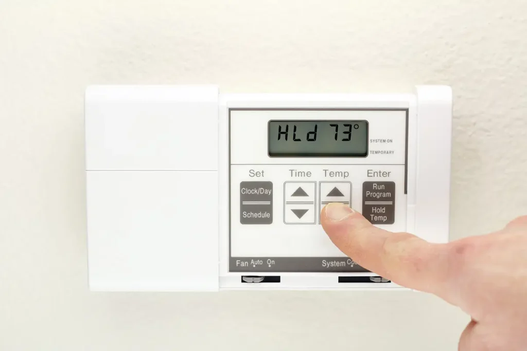 Finger adjusting digital thermostat temperature on wall, showing 73 degrees, for home climate control and energy efficiency.