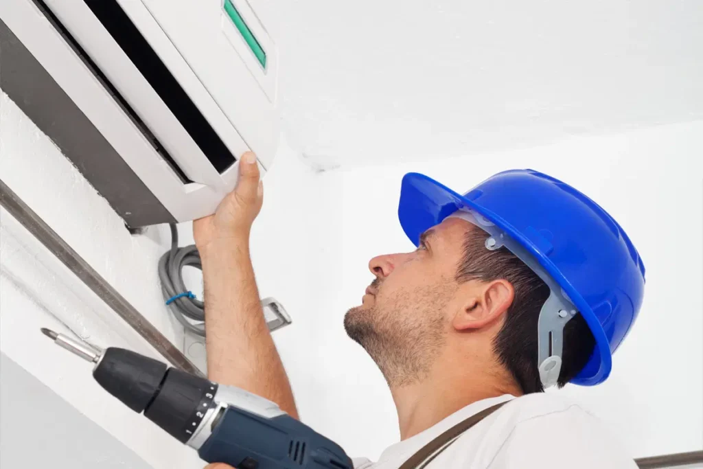 Air conditioning technician in blue hard hat installing unit with drill.