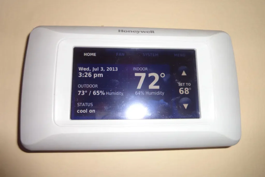 Smart thermostat display showing indoor temperature 72°F, outdoor 73°F, humidity levels, and cooling status.