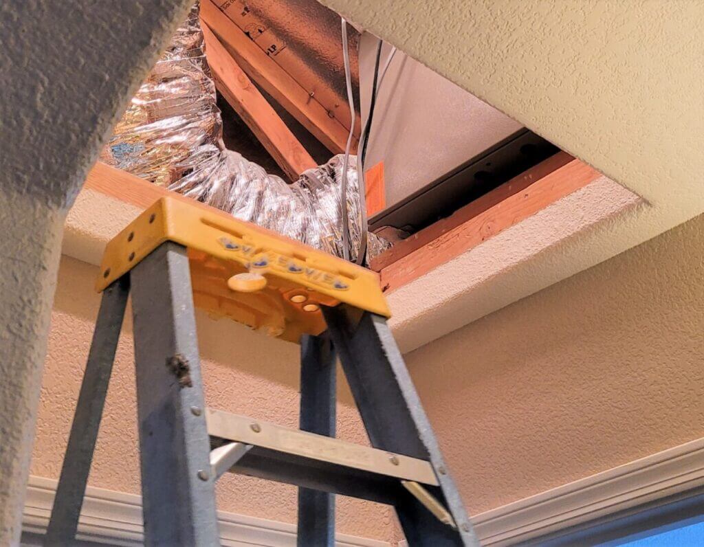HVAC technician installing coil in attic with ladder, ductwork visible, residential heating and cooling maintenance.